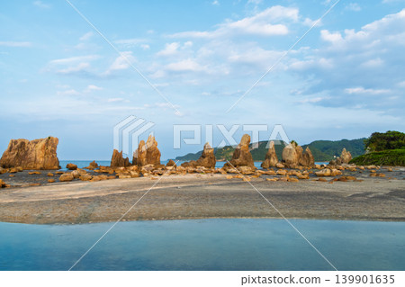 The Hashigui-iwa rocks of Wakayama Prefecture line up in a straight line along the coast under a beautiful blue sky. The Hashigui-iwa rocks of Wakayama Prefecture line up in a straight line along the coast under a beautiful blue sky. 139901635