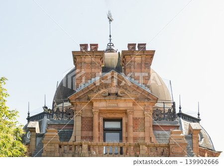Crowning the rooftop of Greenwich's Altazimuth Pavilion, an ornate red-brick and terracotta facade exemplifies late Victorian craftsmanship. The central pediment features a detailed relief bust of Crowning the rooftop of Greenwich's Altazimuth Pavilion, an ornate red-brick and terracotta facade exemplifies late Victorian craftsmanship. The central pediment features a detailed relief bust of 139902666