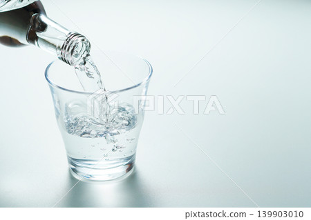 將瓶裝礦泉水倒入玻璃杯中。 將瓶裝礦泉水倒入玻璃杯中。 139903010