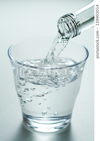 將瓶裝礦泉水倒入玻璃杯中。 將瓶裝礦泉水倒入玻璃杯中。 139903014