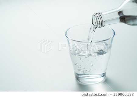 將瓶裝礦泉水倒入玻璃杯中。 將瓶裝礦泉水倒入玻璃杯中。 139903157