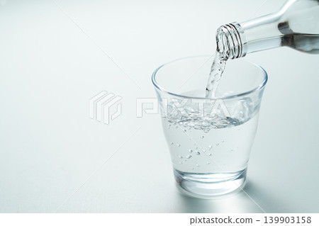 將瓶裝礦泉水倒入玻璃杯中。 將瓶裝礦泉水倒入玻璃杯中。 139903158