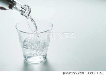 將瓶裝礦泉水倒入玻璃杯中。 將瓶裝礦泉水倒入玻璃杯中。 139903159