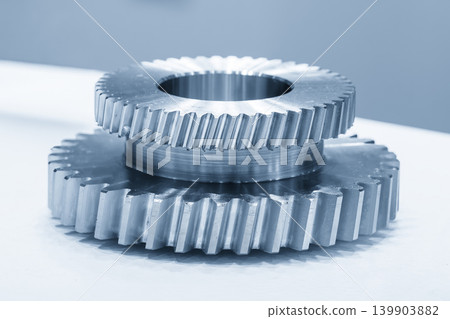 Close-up of two different sizes of precision bevel gear parts placed on a steel metal ring component in a blue-toned scene. Close-up of two different sizes of precision bevel gear parts placed on a steel metal ring component in a blue-toned scene. 139903882
