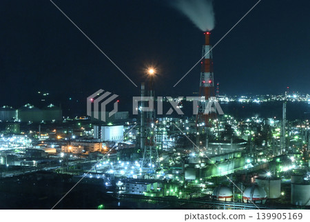 An industrial landscape featuring chimneys and glittering factory complexes at night. 139905169