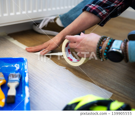 Girl Applying Painting Tape for Flooring Project Indoors Girl Applying Painting Tape for Flooring Project Indoors 139905555