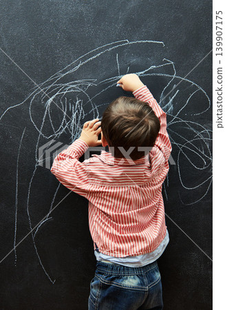Young child, scribble and art on chalkboard in classroom of preschool for education of little boy. Kid, drawing and creative on blackboard with illustration for elementary, student and sketch Young child, scribble and art on chalkboard in classroom of preschool for education of little boy. Kid, drawing and creative on blackboard with illustration for elementary, student and sketch 139907175
