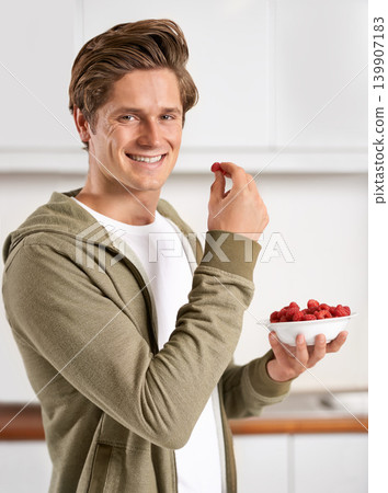 Smile, portrait and man with raspberries in kitchen of home for diet, health and wellness. Happy, confident and male person eating fruit for fresh, organic or nutrition snack in modern apartment. Smile, portrait and man with raspberries in kitchen of home for diet, health and wellness. Happy, confident and male person eating fruit for fresh, organic or nutrition snack in modern apartment. 139907183