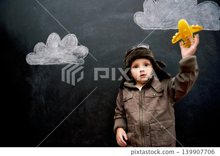 Child, boy and face by blackboard with plane for creative fun, playing or drawing of clouds for imagination. Student, kid and confidence with airplane, chalkboard or illustration for knowledge or sky Child, boy and face by blackboard with plane for creative fun, playing or drawing of clouds for imagination. Student, kid and confidence with airplane, chalkboard or illustration for knowledge or sky 139907706