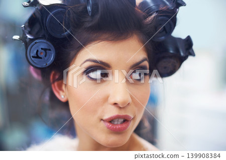 Woman, face and hair curlers with makeup for beauty in salon with haircare, self care or cosmetology. Model, person or hairstyle for morning routine, curling or getting ready for wellness or grooming Woman, face and hair curlers with makeup for beauty in salon with haircare, self care or cosmetology. Model, person or hairstyle for morning routine, curling or getting ready for wellness or grooming 139908384