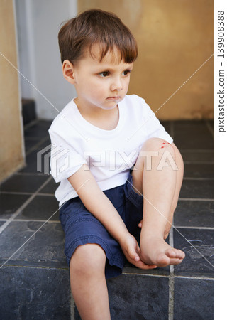 Little boy, sitting and injury on knee in home and accident, ache and with blood from cut. Young child, sad and holding hurt leg up with hand on foot, pain and sore on bruise with fear of trouble Little boy, sitting and injury on knee in home and accident, ache and with blood from cut. Young child, sad and holding hurt leg up with hand on foot, pain and sore on bruise with fear of trouble 139908388