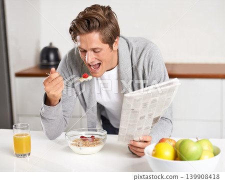 Cereal, juice and man with newspaper in kitchen for information at modern apartment. Nutrition, breakfast and young male person drinking healthy beverage and reading journalism article at home. Cereal, juice and man with newspaper in kitchen for information at modern apartment. Nutrition, breakfast and young male person drinking healthy beverage and reading journalism article at home. 139908418