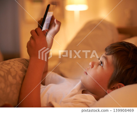 Boy, kid and tablet in bedroom at night for typing, reading or online game with app in family home. Child, bed and digital touchscreen for movie, cartoon and streaming subscription to relax in house Boy, kid and tablet in bedroom at night for typing, reading or online game with app in family home. Child, bed and digital touchscreen for movie, cartoon and streaming subscription to relax in house 139908469