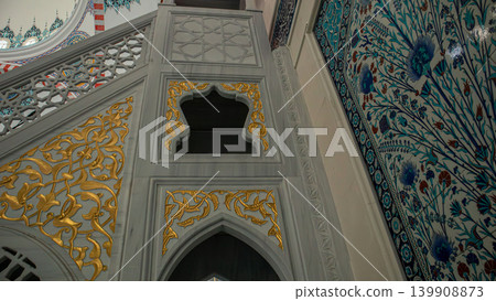 Inside the mosque, the wall features intricate floral tiles in Iznik style. The blue and red tulip designs add character to the sacred place. Visitors admire the craftsmanship and artistry. 139908873
