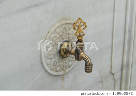 Ornate brass faucet is mounted on a carved marble surface. This design is typical in Islamic architecture related to water features and fountains. This style shows craftsmanship. 139908878