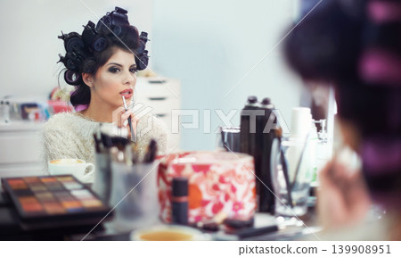 Woman, face and hair curlers or lipstick for beauty in mirror with haircare, self care or cosmetology. Model, person or hairstyle for morning routine, makeup or getting ready for wellness or grooming Woman, face and hair curlers or lipstick for beauty in mirror with haircare, self care or cosmetology. Model, person or hairstyle for morning routine, makeup or getting ready for wellness or grooming 139908951