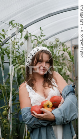 A seductive girl collects organic tomatoes in a greenhouse in the village, is engaged in farming. A seductive girl collects organic tomatoes in a greenhouse in the village, is engaged in farming. 139909918