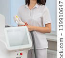 Cosmetologist in white uniform holding a laser handpiece 139910647