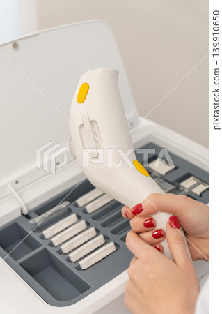 professional hands with red nails changing a cartridge on a white laser hair removal device 139910650