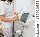 Professional cosmetologist operating a modern laser machine in a bright clinic. 139910653