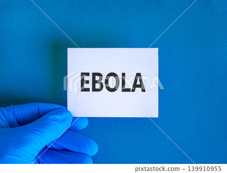 Ebola virus medical words symbol. Concept word Ebola on beautiful white paper. Beautiful blue background. Doctor hand in blue medical glove. Medical Ebola virus concept. Copy space. Ebola virus medical words symbol. Concept word Ebola on beautiful white paper. Beautiful blue background. Doctor hand in blue medical glove. Medical Ebola virus concept. Copy space. 139910955