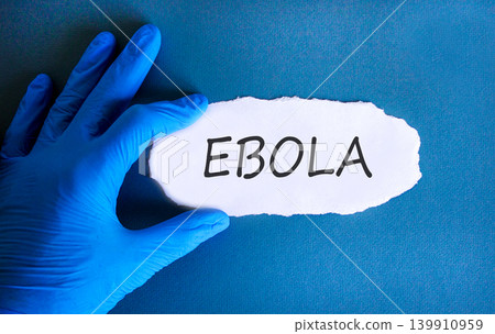 Ebola virus medical words symbol. Concept word Ebola on beautiful white paper. Beautiful blue background. Doctor hand in blue medical glove. Medical Ebola virus concept. Copy space. Ebola virus medical words symbol. Concept word Ebola on beautiful white paper. Beautiful blue background. Doctor hand in blue medical glove. Medical Ebola virus concept. Copy space. 139910959