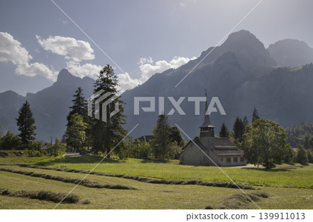 Alpine church in green meadow with towering mountains Alpine church in green meadow with towering mountains 139911013
