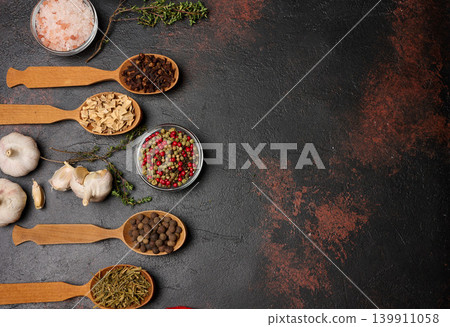 Spices on a dark background in wooden spoons: pepper, cloves, ginger, allspice and bay leaf, salt, thyme. Top view Spices on a dark background in wooden spoons: pepper, cloves, ginger, allspice and bay leaf, salt, thyme. Top view 139911058