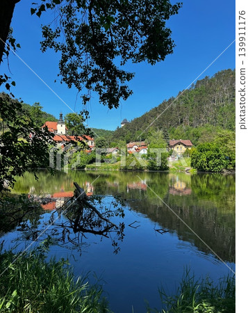 Scenic view of a tranquil river reflecting a small village surrounded by 139911176