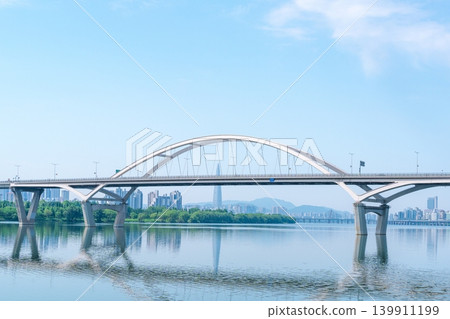 Beautiful yellow canola flowers (rapeseed) blooming along the Han River with Guri-Amsa Bridge in the background on a sunny spring afternoon Beautiful yellow canola flowers (rapeseed) blooming along the Han River with Guri-Amsa Bridge in the background on a sunny spring afternoon 139911199