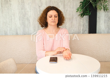 Middle-aged woman checking her pulse at a cafe table for self care and health monitoring Middle-aged woman checking her pulse at a cafe table for self care and health monitoring 139911215