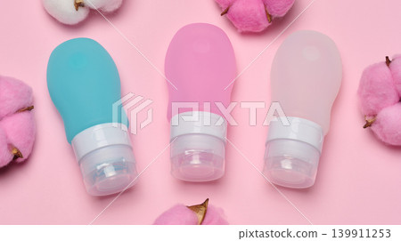 Three multi-colored travel cosmetic bottles lie surrounded by soft cotton flowers Three multi-colored travel cosmetic bottles lie surrounded by soft cotton flowers 139911253