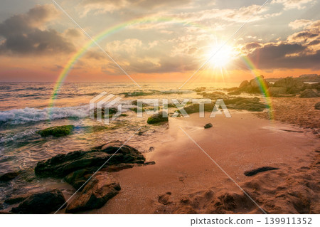sunset over huge stones on a sandy beach. wonderful summer vacation season at the black sea. calm waves washing the sand shore. nature background with cloudy sky. weather with rainbow sunset over huge stones on a sandy beach. wonderful summer vacation season at the black sea. calm waves washing the sand shore. nature background with cloudy sky. weather with rainbow 139911352
