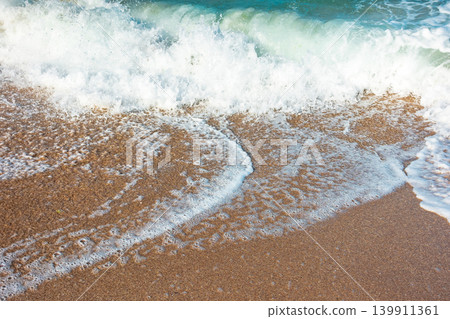 sea wave rolling foam on to the sandy beach. nature background on a sunny day. closeup texture of sea, sand, water and foam. seaside environment. tide on seashore 139911361