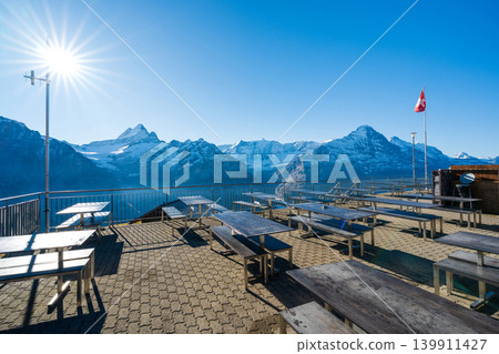 Outdoor terrace seating at Berggasthaus First, overlooking the Eiger peak, and the Swiss flag. Grindelwald, Bern. Outdoor terrace seating at Berggasthaus First, overlooking the Eiger peak, and the Swiss flag. Grindelwald, Bern. 139911427
