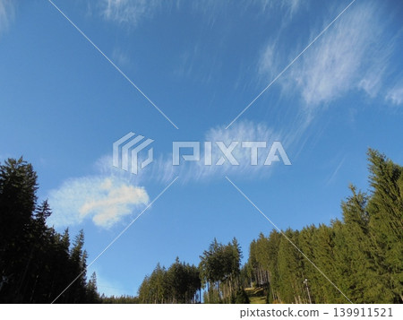 Beautiful sparse clouds on a blue sky over mountain forests. Beautiful sparse clouds on a blue sky over mountain forests. 139911521