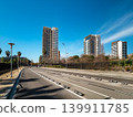 Urban landscape featuring modern skyscrapers along a clear road under a blue sky. Palm trees line the street, creating a vibrant city atmosphere. 139911785