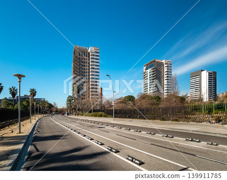 Urban landscape featuring modern skyscrapers along a clear road under a blue sky. Palm trees line the street, creating a vibrant city atmosphere. 139911785