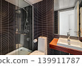 Modern bathroom with a glass shower, sleek sink, and dark tiled walls. The space is well-lit and features contemporary design elements. 139911787