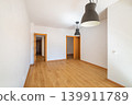 Empty room with wooden floor, white walls, and two pendant lights. Doors lead to other spaces. Bright and spacious atmosphere. 139911789