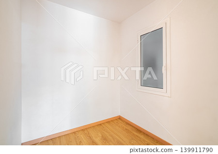 Empty room with white walls and a wooden floor. A single window is present, allowing natural light to enter the space Empty room with white walls and a wooden floor. A single window is present, allowing natural light to enter the space 139911790