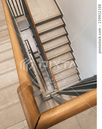 Wooden railing frames view down staircase in contemporary building. Clean lines and elegant design elements within bright space. Decorative for architecture themes 139912108