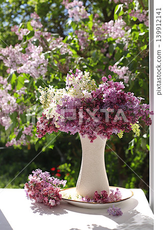 Beautiful spring lilac branches in a vase on a sunny windowsill, abstract floral arrangement, home interior with decorative elements, still life with flowers of different varieties of lilac, Beautiful spring lilac branches in a vase on a sunny windowsill, abstract floral arrangement, home interior with decorative elements, still life with flowers of different varieties of lilac, 139912141