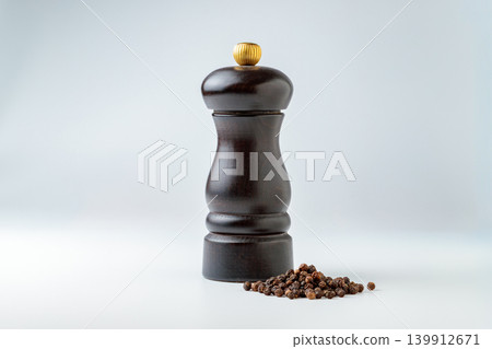 一張調味品照片，照片中可以看到一個木製胡椒研磨器和黑胡椒粒，背景是白色。 139912671