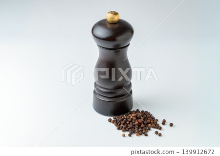 從上方斜角拍攝的照片，顯示了白色背景上的木製胡椒研磨器和黑胡椒粒。 139912672