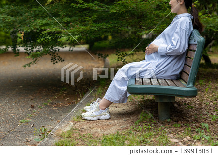 一位挺著大肚子的孕婦正坐在公園長椅上休息。 139913031
