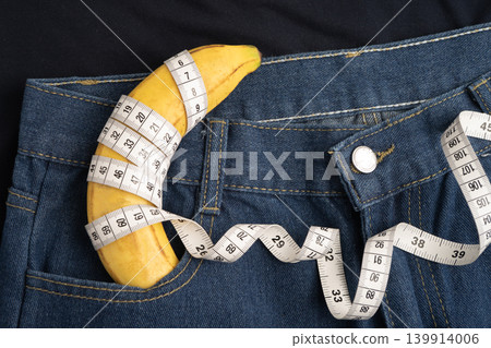 Banana with measuring tape on jean trousers, penis health. Banana with measuring tape on jean trousers, penis health. 139914006