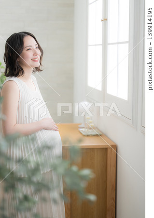 A smiling Japanese pregnant woman places her hand on her stomach; a smile representing the maternity lifestyle. A smiling Japanese pregnant woman places her hand on her stomach; a smile representing the maternity lifestyle. 139914195
