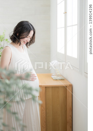A Japanese pregnant woman with a smile and her hand on her stomach, a maternity lifestyle image with a downcast smile. A Japanese pregnant woman with a smile and her hand on her stomach, a maternity lifestyle image with a downcast smile. 139914196