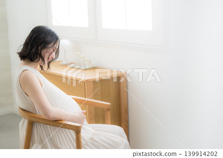 A Japanese pregnant woman smiles and places her hand on her stomach; a smiling, back view of a maternity lifestyle image. A Japanese pregnant woman smiles and places her hand on her stomach; a smiling, back view of a maternity lifestyle image. 139914202
